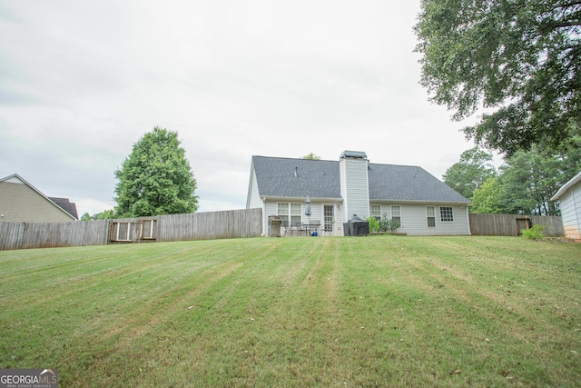 rear view of property with a lawn, a chimney, and a fenced backyard