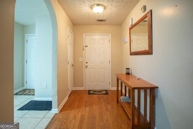 doorway to outside with visible vents, baseboards, light wood finished floors, arched walkways, and a textured ceiling