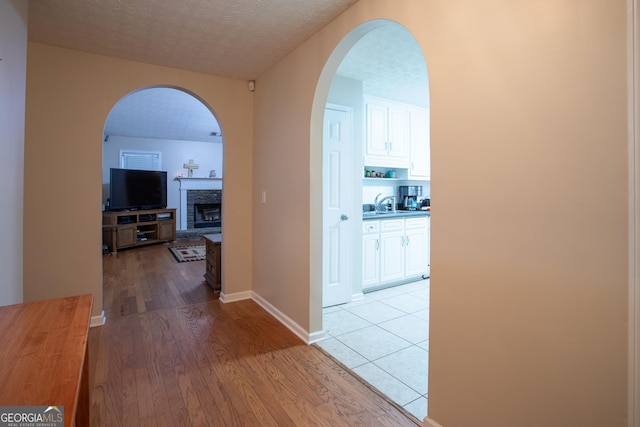 hallway with light wood-style flooring, a sink, a textured ceiling, arched walkways, and baseboards