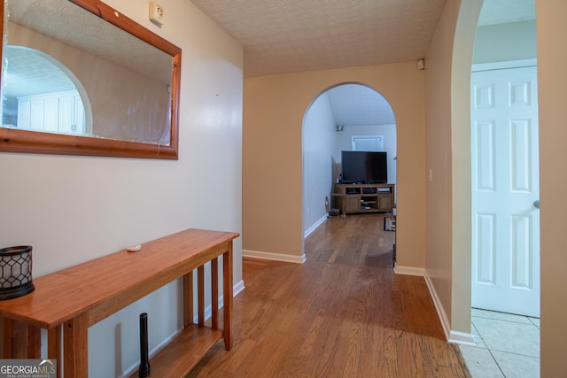 hallway with baseboards, arched walkways, a textured ceiling, and wood finished floors