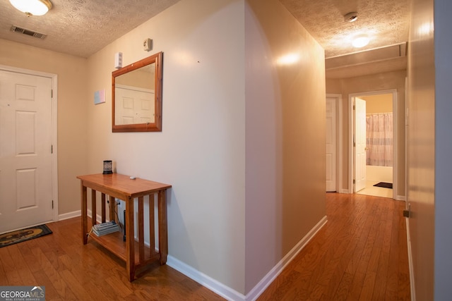 hall with hardwood / wood-style flooring, baseboards, visible vents, and a textured ceiling