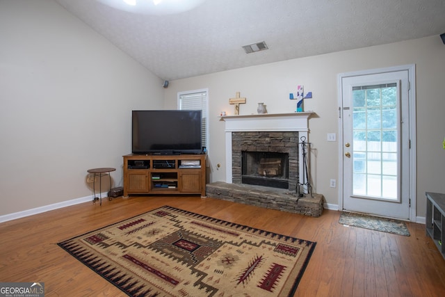 living area featuring visible vents, hardwood / wood-style flooring, a textured ceiling, a stone fireplace, and lofted ceiling