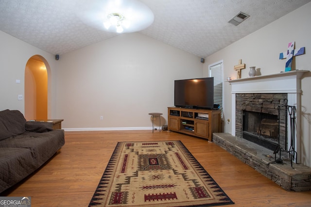 living room with vaulted ceiling, visible vents, light wood finished floors, and a textured ceiling