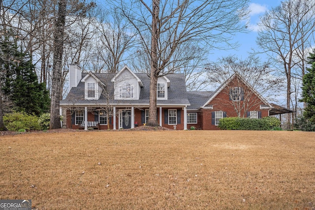 cape cod house with brick siding, a shingled roof, a front yard, covered porch, and a chimney