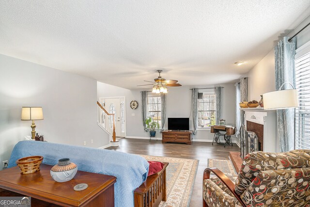 living room featuring a tiled fireplace, a textured ceiling, wood finished floors, baseboards, and stairs