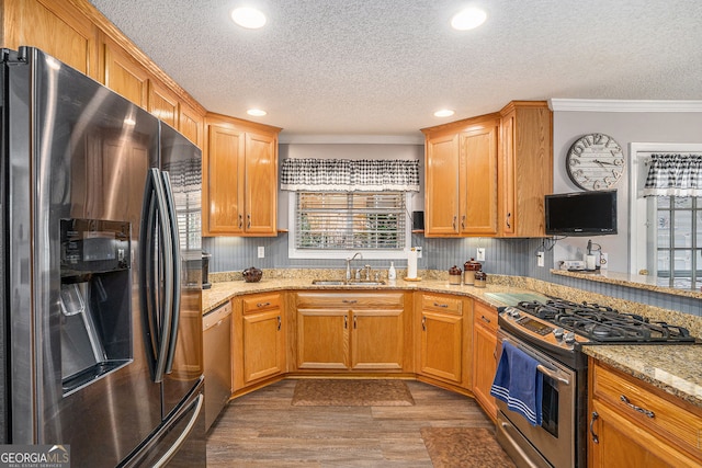 kitchen with light stone counters, appliances with stainless steel finishes, wood finished floors, a textured ceiling, and a sink