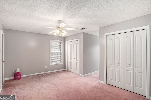 unfurnished bedroom featuring light colored carpet, visible vents, two closets, and baseboards