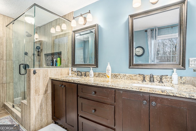 bathroom featuring a textured ceiling, double vanity, a stall shower, and a sink