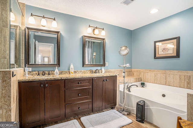 bathroom featuring wood finished floors, visible vents, double vanity, a sink, and a bath