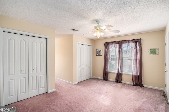 unfurnished bedroom with visible vents, two closets, a textured ceiling, carpet floors, and baseboards