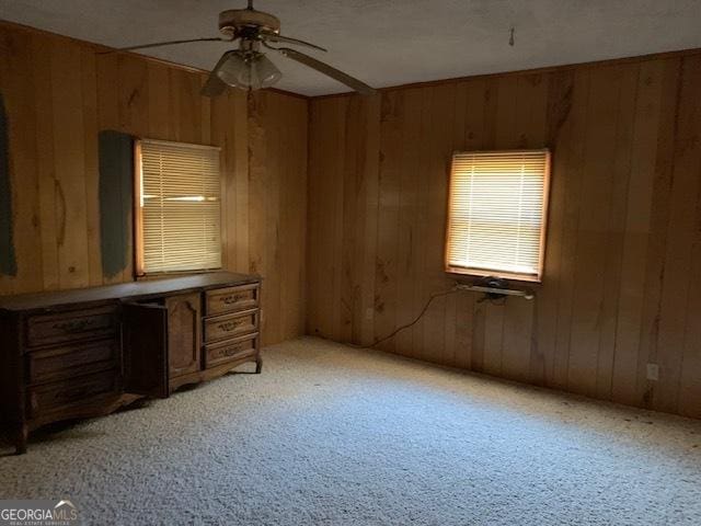 interior space featuring light carpet, wooden walls, and ceiling fan