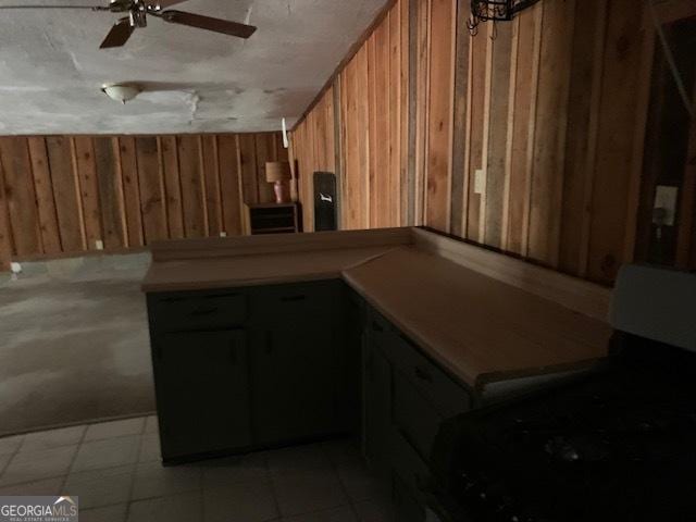 kitchen featuring wood walls, gas range oven, a peninsula, brown cabinetry, and a ceiling fan