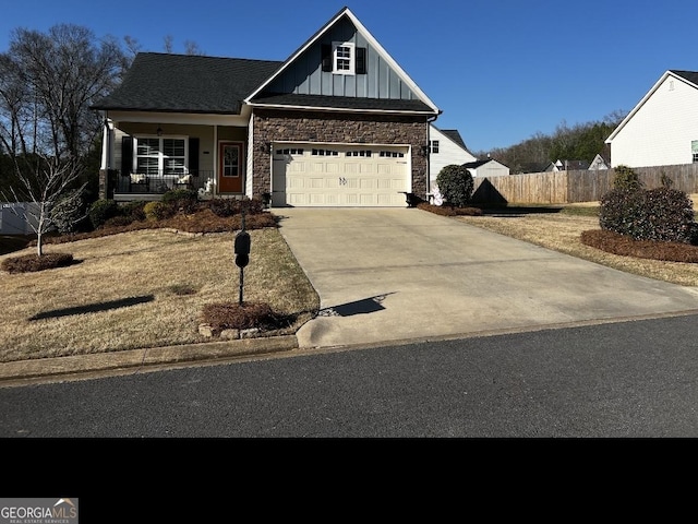 view of front of house with board and batten siding, fence, a porch, concrete driveway, and stone siding