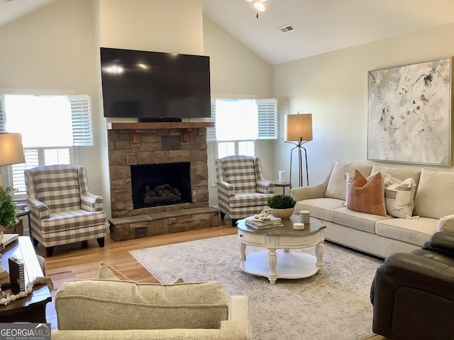 living area featuring a stone fireplace, a healthy amount of sunlight, wood finished floors, and vaulted ceiling