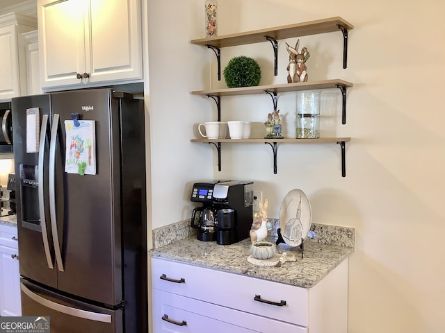 kitchen with light stone counters, white cabinets, fridge with ice dispenser, and open shelves