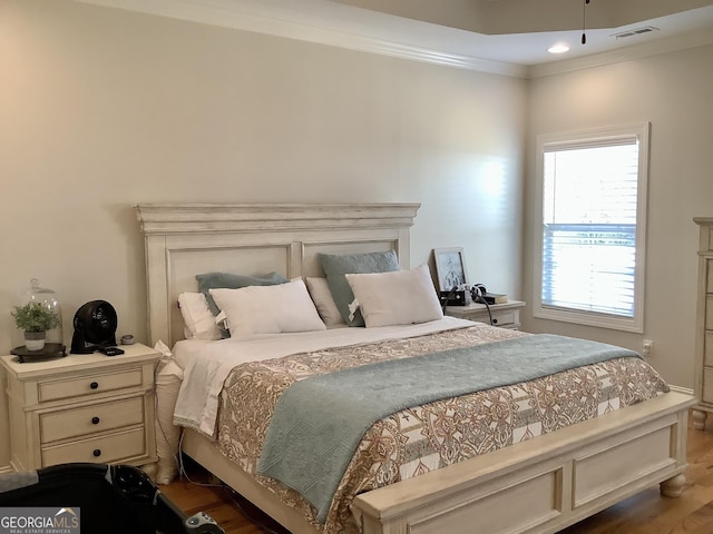 bedroom featuring wood finished floors, visible vents, and ornamental molding