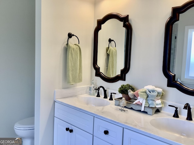 bathroom with a sink, toilet, and double vanity