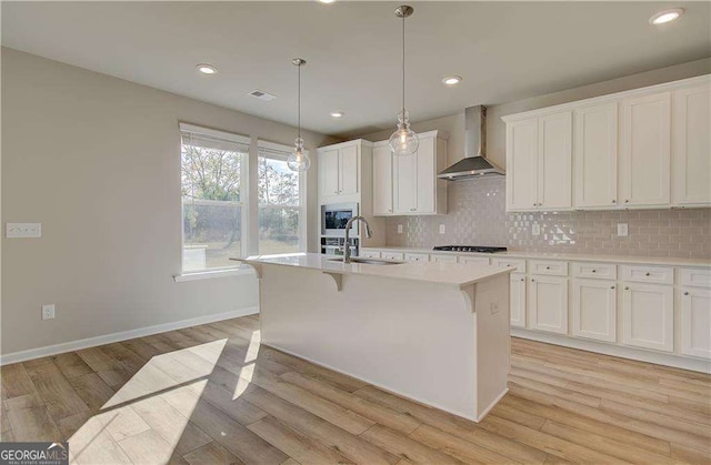 kitchen with an island with sink, a sink, backsplash, wall chimney exhaust hood, and built in microwave