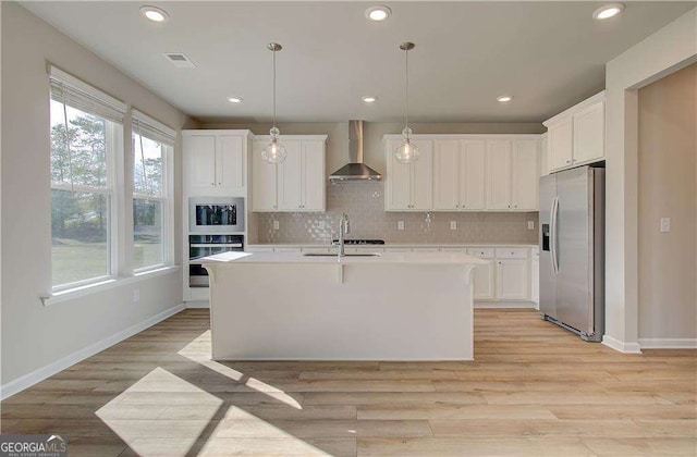 kitchen featuring decorative backsplash, appliances with stainless steel finishes, light countertops, and wall chimney exhaust hood