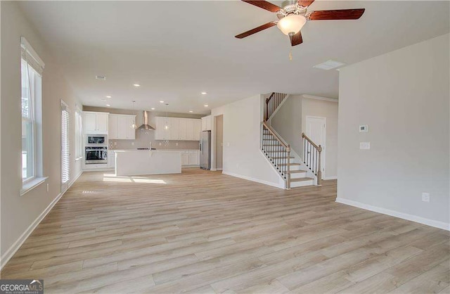 unfurnished living room featuring stairway, baseboards, and light wood-style floors