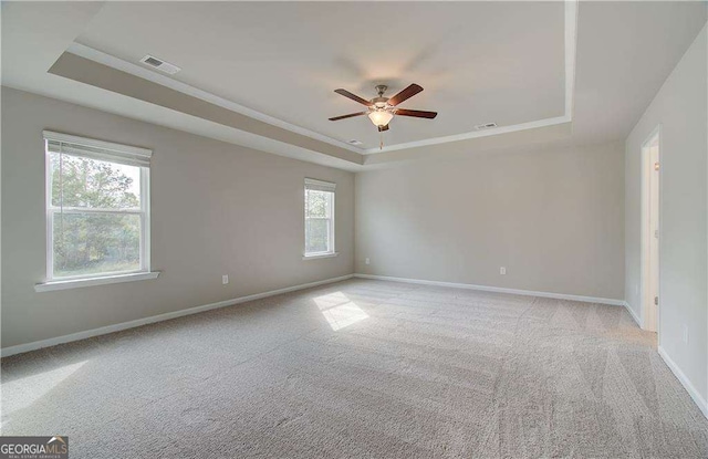 unfurnished room featuring visible vents, a ceiling fan, baseboards, a raised ceiling, and light colored carpet