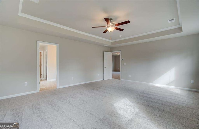 empty room featuring crown molding, baseboards, light colored carpet, a tray ceiling, and a ceiling fan