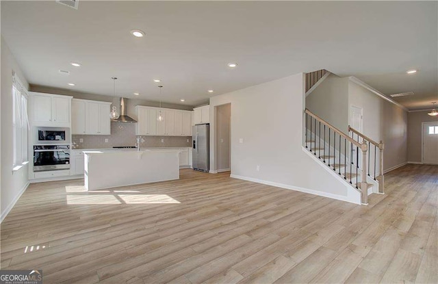 kitchen featuring light countertops, appliances with stainless steel finishes, white cabinetry, wall chimney exhaust hood, and open floor plan