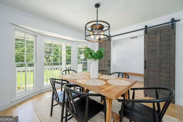 dining area with a barn door, plenty of natural light, light wood-style floors, and ornamental molding