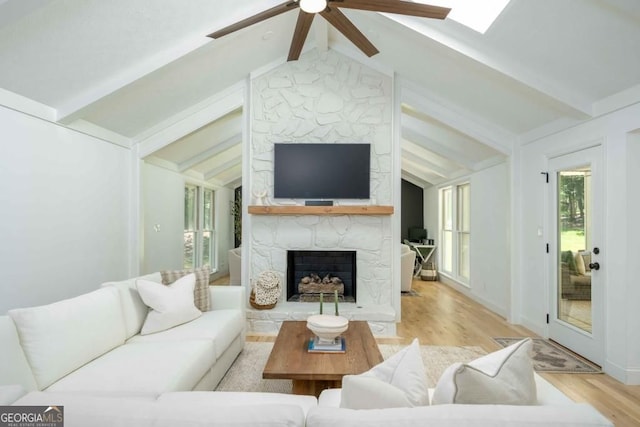 living area with lofted ceiling with beams, light wood-style floors, and a stone fireplace