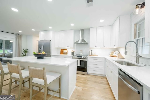 kitchen with a breakfast bar area, visible vents, a sink, stainless steel appliances, and wall chimney range hood