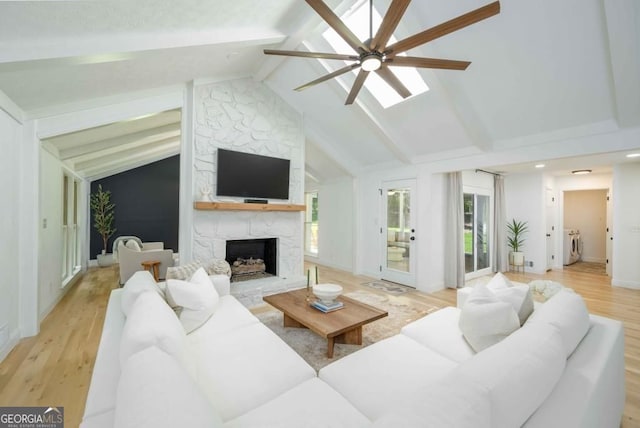 living area featuring light wood finished floors, ceiling fan, beam ceiling, a fireplace, and a skylight