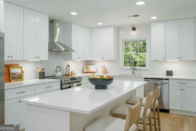 kitchen with a breakfast bar area, visible vents, a sink, appliances with stainless steel finishes, and wall chimney range hood