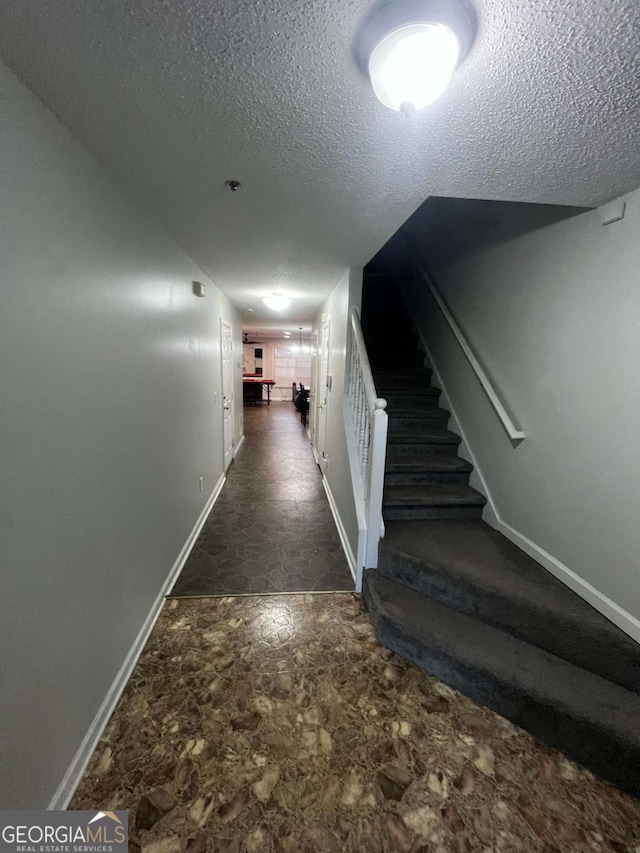 hall with stairway, stone finish flooring, baseboards, and a textured ceiling