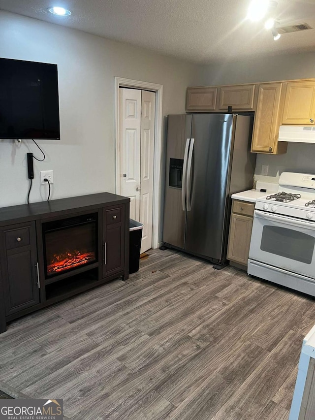 kitchen featuring wood finished floors, white range with gas cooktop, stainless steel refrigerator with ice dispenser, under cabinet range hood, and a textured ceiling