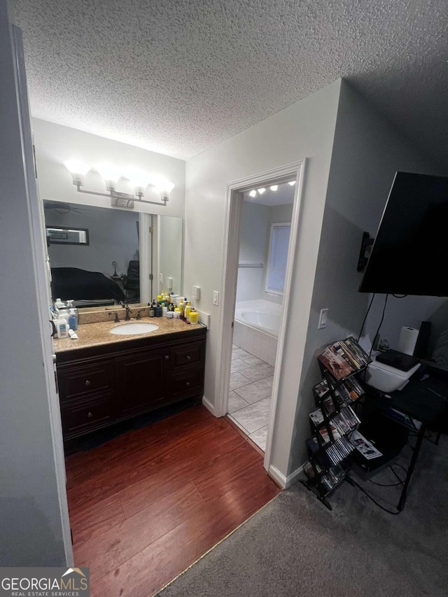 full bathroom with a bath, a textured ceiling, vanity, and wood finished floors