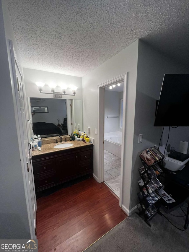 full bathroom featuring a bathing tub, a textured ceiling, wood finished floors, and vanity