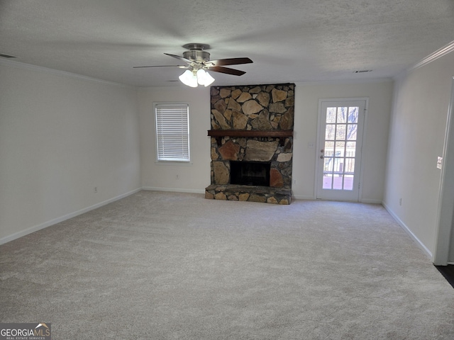 unfurnished living room with baseboards, carpet floors, a stone fireplace, a textured ceiling, and crown molding