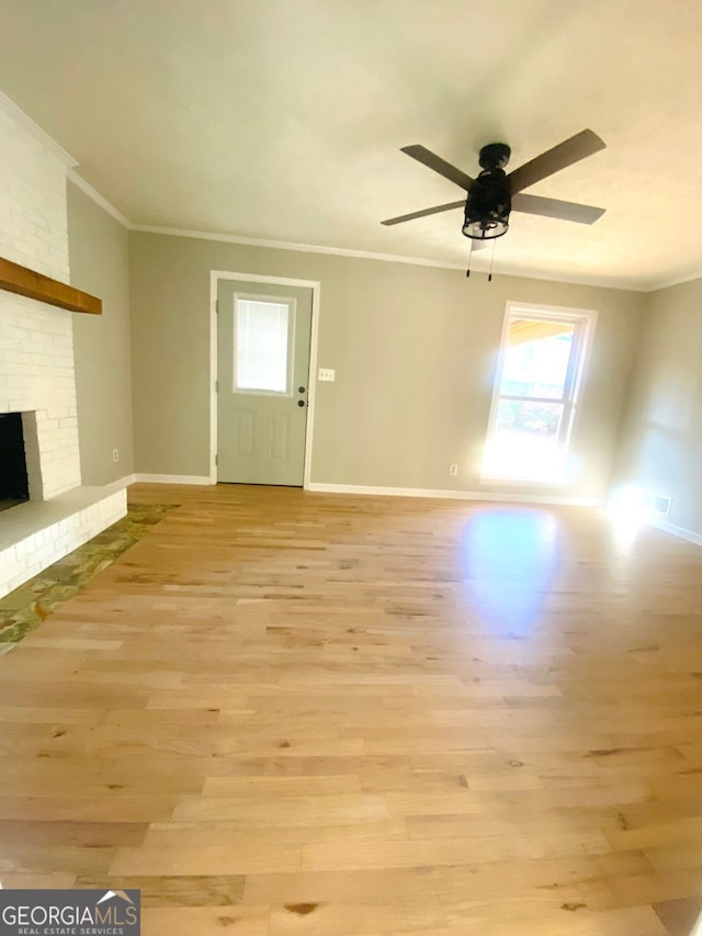 unfurnished living room with crown molding, a brick fireplace, a ceiling fan, and light wood finished floors