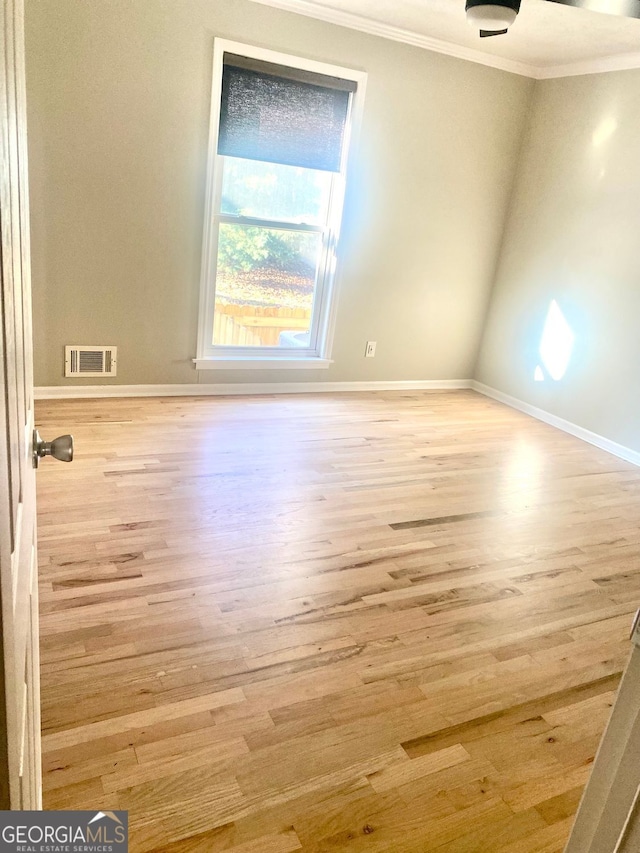 spare room featuring crown molding, wood finished floors, visible vents, and baseboards