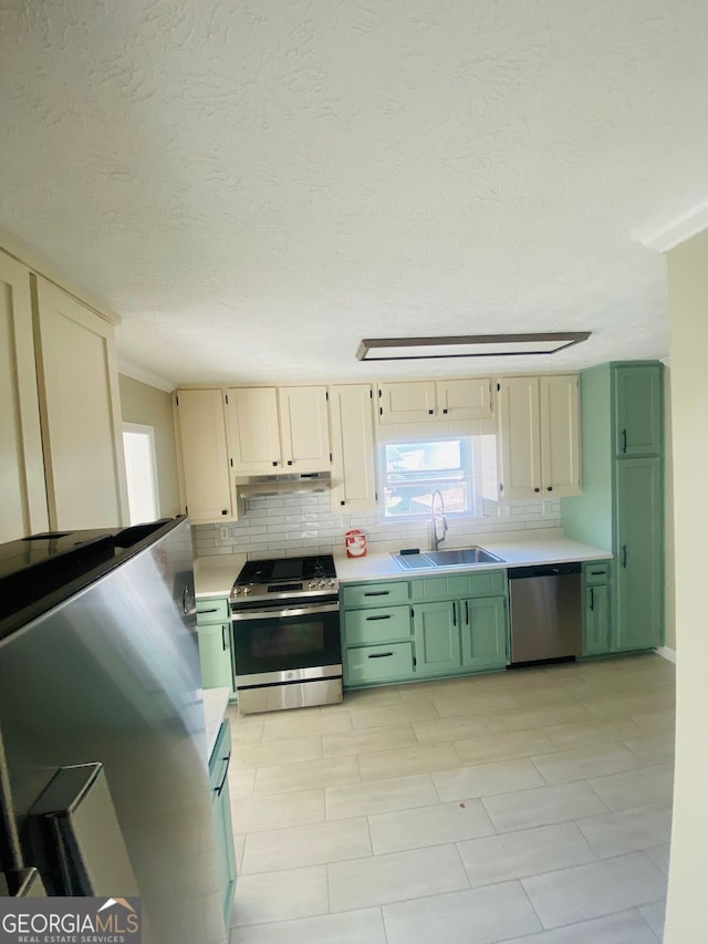 kitchen with under cabinet range hood, green cabinetry, light countertops, appliances with stainless steel finishes, and a sink