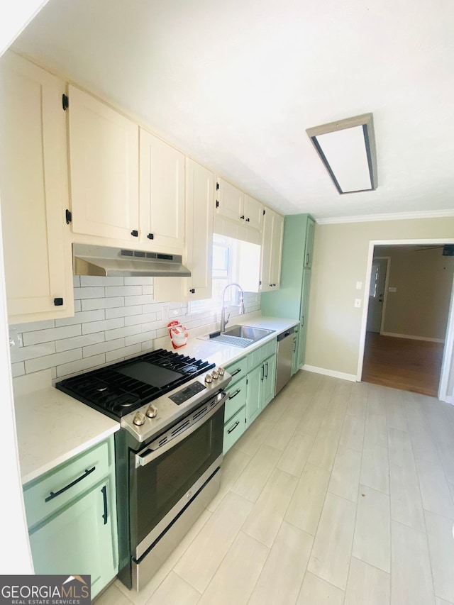 kitchen with tasteful backsplash, under cabinet range hood, green cabinetry, appliances with stainless steel finishes, and a sink