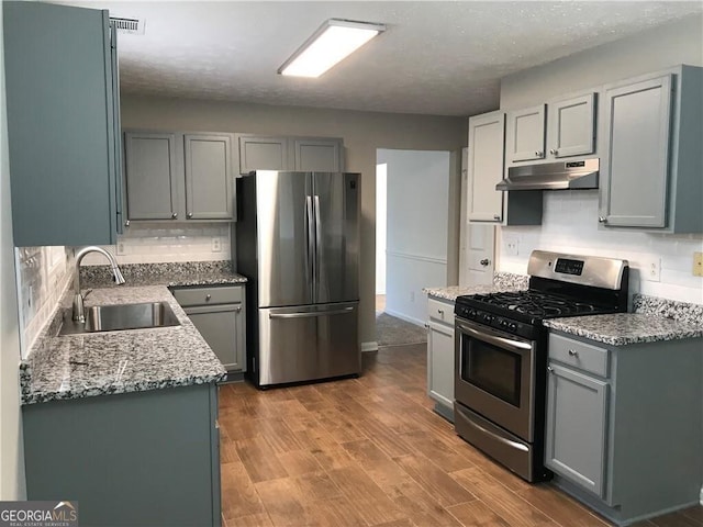 kitchen featuring under cabinet range hood, gray cabinets, wood finished floors, stainless steel appliances, and a sink