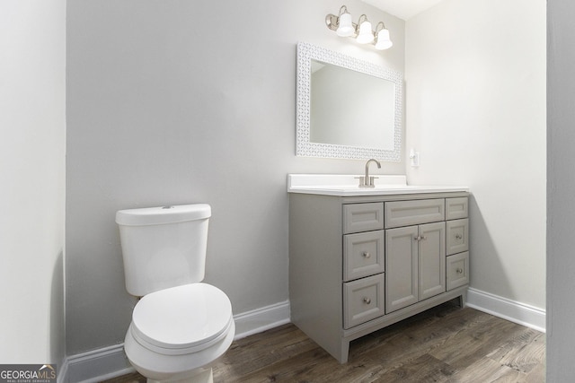 half bath with baseboards, toilet, wood finished floors, and vanity