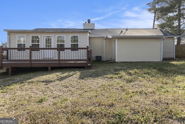 back of property with fence, a chimney, a deck, central air condition unit, and a lawn