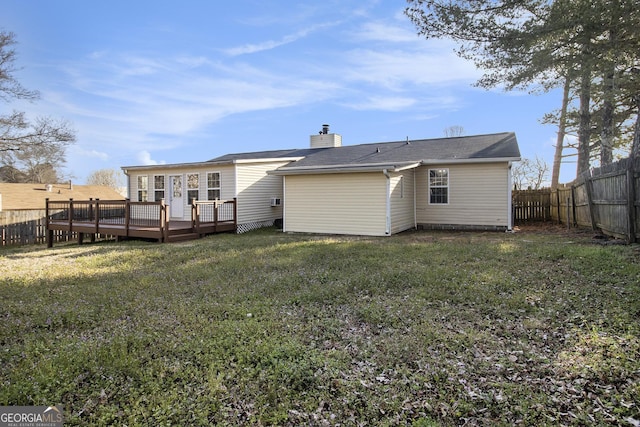 back of property with a yard, a chimney, a wooden deck, and a fenced backyard