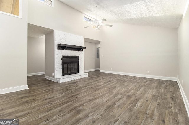 unfurnished living room featuring baseboards, ceiling fan, dark wood finished floors, a stone fireplace, and a textured ceiling