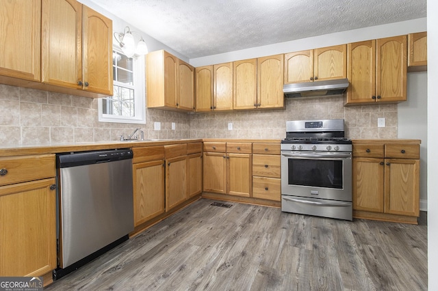 kitchen with under cabinet range hood, a sink, wood finished floors, stainless steel appliances, and light countertops