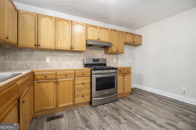 kitchen featuring wood finished floors, visible vents, stainless steel range with gas cooktop, under cabinet range hood, and backsplash