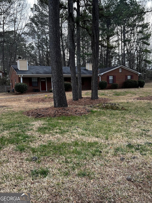 view of front of home featuring brick siding, a chimney, and a front yard