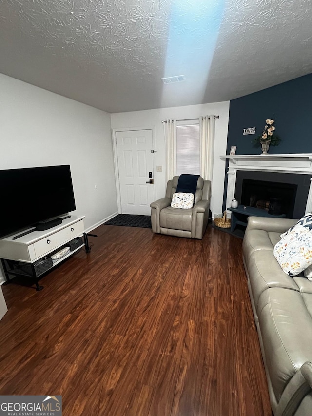 living room with visible vents, a fireplace with raised hearth, a textured ceiling, and wood finished floors